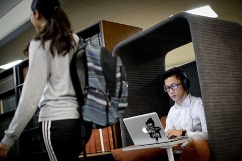 Student studying on a laptop in the library while anoter student walks by