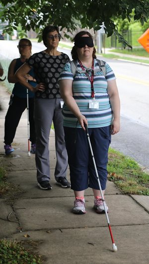 Student practicing using a white cane on the sidewalk