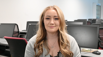 Student Bridgid Harkin shown in grey sweater seated in a computer lab.