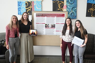 SLP students smiling in front of their capstone poster