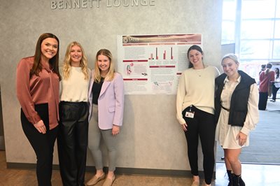 4 SLP students with their advisor standing in front of their capstone poster