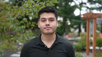 Student Fernando Venegas shown in black button up shirt with blurred greenery in the background.