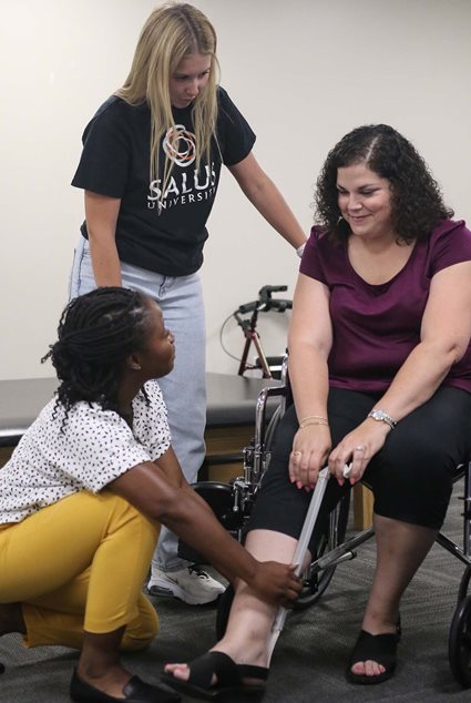 Salus OT students helping a patient learn to put on shoes independently