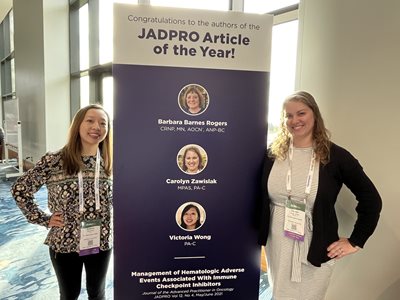 Victoria Wong and her coworker standing in front of a poster recognizing their article of the year