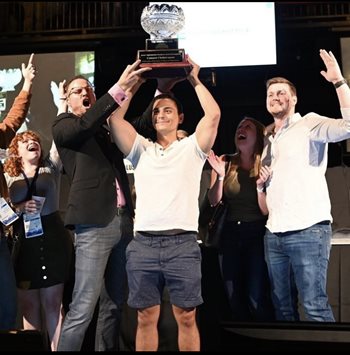 Tyler Lesko holding trophy as quiz bowl champion surrounded by cheering crowd at Optometry's Meeting 2021