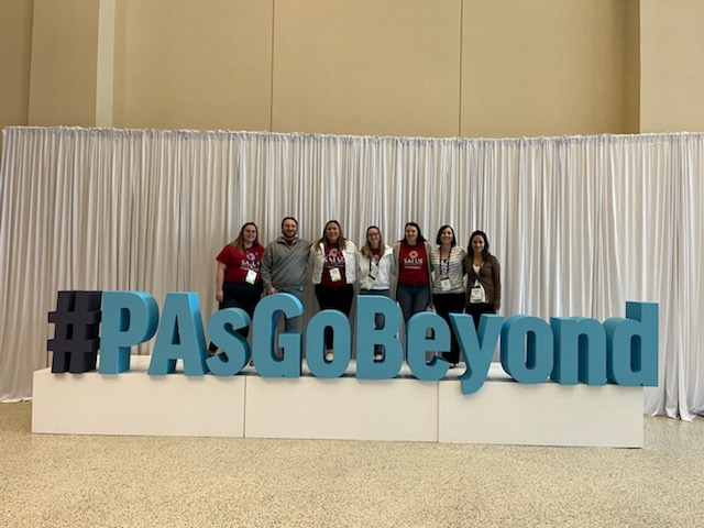 PA faculty and staff standing in front of a sign that says "PA's Go Beyond"