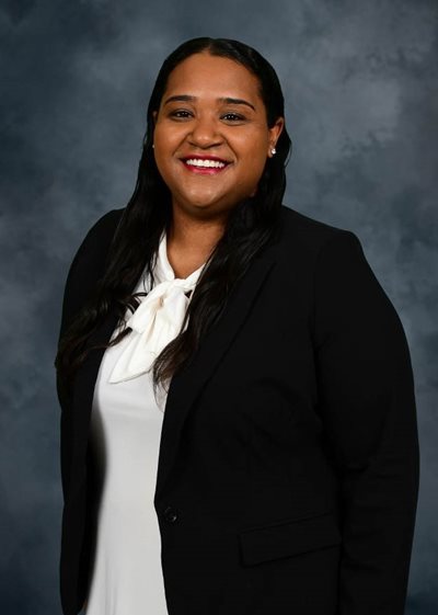 Kelsi Jones headshot wearing a white shirt and black blazer standing in front of a grey background