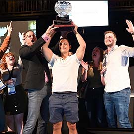 Tyler Lesko holding trophy as quiz bowl champion surrounded by cheering crowd at Optometry's Meeting 2021