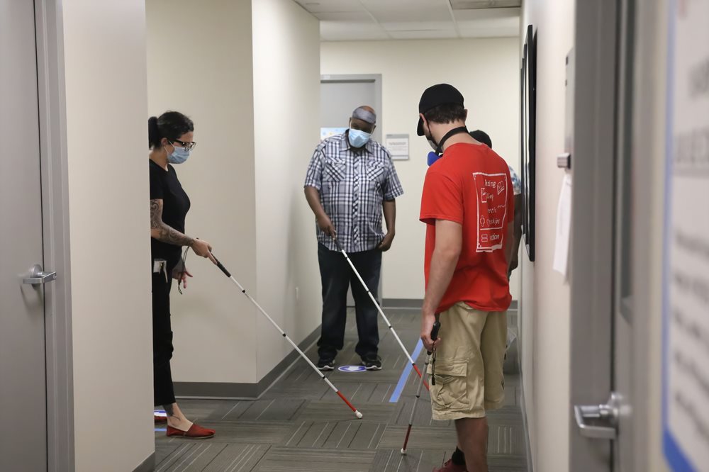 students practicing using white cane in a campus hallway