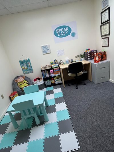 Photo of SpeakEasy Therapy, a desk in the far back right corner, a small table on the left and posters along the wall