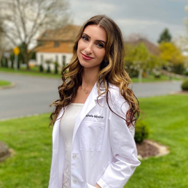 Michelle Mikviman standing outside smiling wearing a white coat and white dress