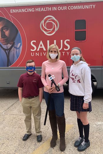 Photo of LOFK host NBC10 news anchor and reporter Rosemary Connors with two local children in front of the University's mobile eye clinic.