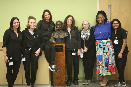 Feinbloom staff standing and smiling with the William Feinbloom statue