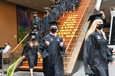 grads walking into the venue, one student holding two thumbs up