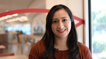 Student Devora Soto shown smiling in front of a window of the Salus library.