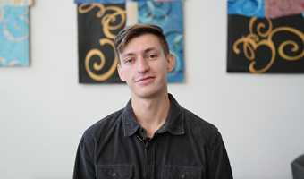 Student Eddie Diaz Serrano shown in black collard shirt in white room with modern art designs in the background.