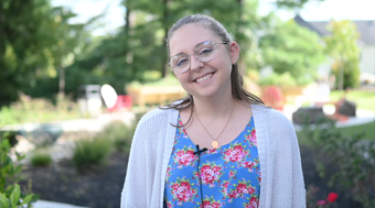 Student Elizabeth Lyter shown in blue shirt with floral design and white cardigan and with blurred greenery in background.