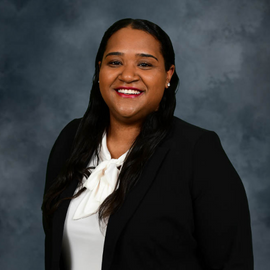 Headshot of Kelsi Jones wearing a white shirt and black blazer standing in front of a grey background