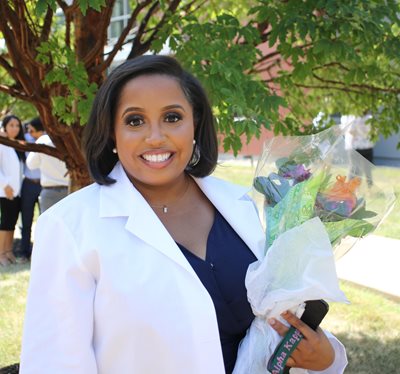 Makayla Cain standing outside the hafter center wearing her white coat and holding a bouquet of flowers