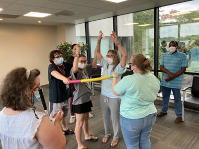 TVI students creating a human helium atom using a hula hoop as the nucleus and brailled note cards indicating which students were to be the protons, neutrons, and electrons. The students in the center of the hula hoop are protons and neutrons and the students holding the outside of the hula hoop are the electrons.