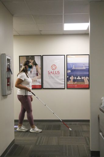 O&M student walking with a mobility stick around the Salus University hallways