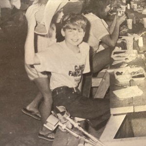 Jeffrey Quelet as a 10 year old shown eating at a picnic table with friends, crutches by his side.