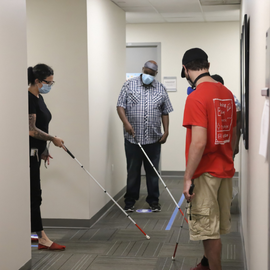 students practicing using white cane in a campus hallway