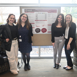 4 SLP students standing in front of their capstone poster smiling