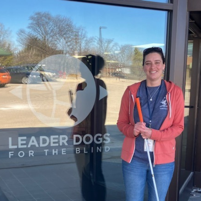 Danielle standing in front of a window holding a white cane