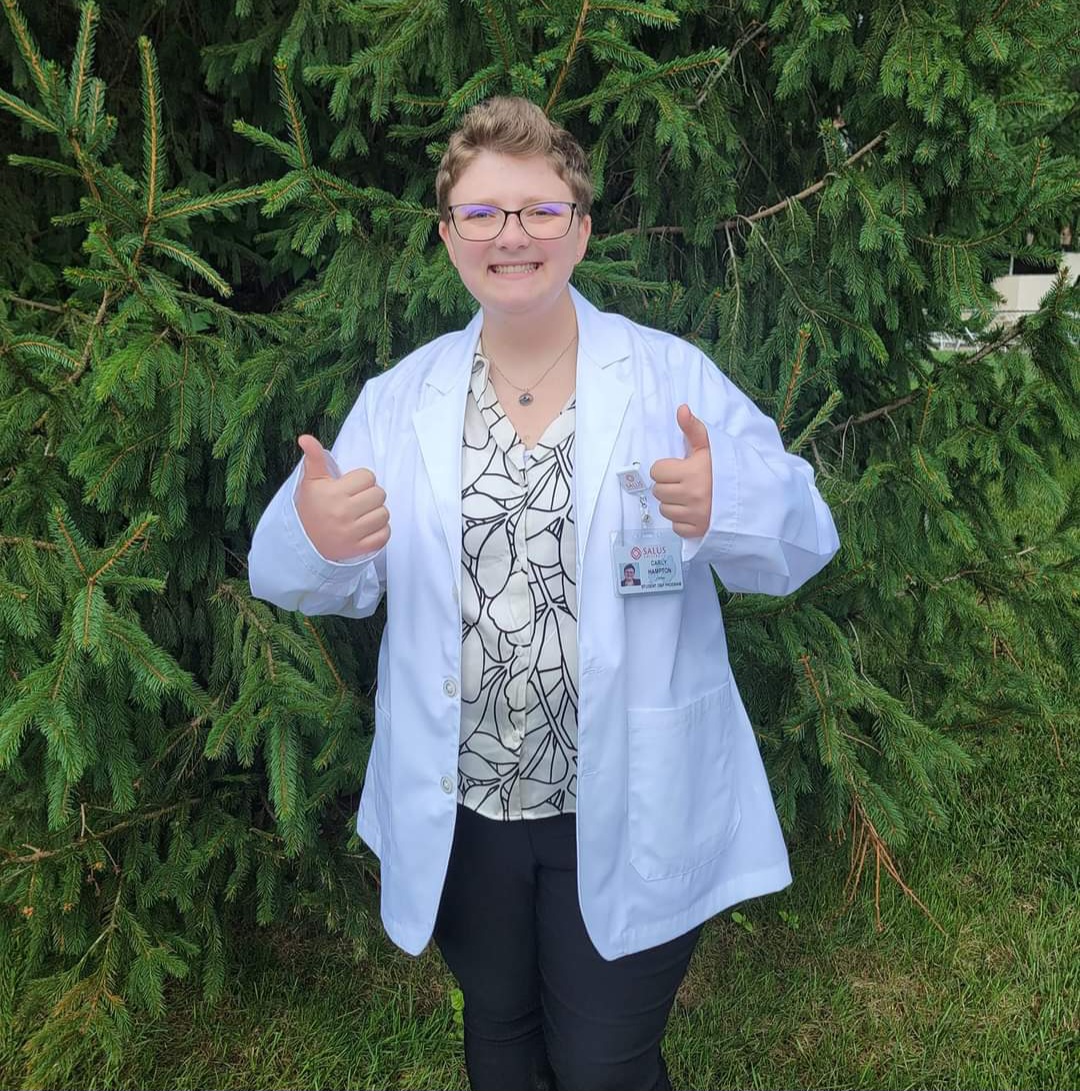 Carly Hampton wearing a white coat holding two thumbs up