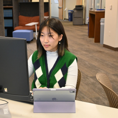 student sitting at computer with ipad in front of her